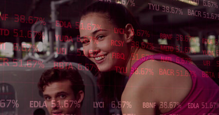 Pausing female wearing pink tank top holding cable machine handle at gym, with stock ticker overlay. Training, fitness, wellness, strength, motivation, gym, activeの写真素材