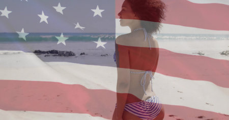 Standing woman wearing blue-striped bikini facing beach shore with US flag overlay, copy space. Patriotism, celebration, adventure, outdoor, leisure, tranquility, vibrantの写真素材
