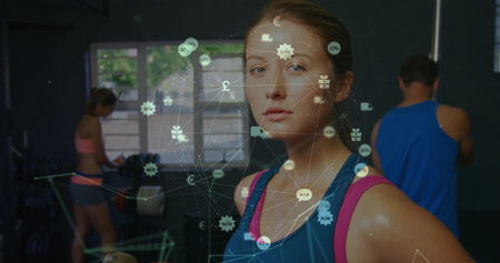 Showing female fitness enthusiast in blue and pink tank standing in gym, with digital icons overlay. Wellness, strength, training, digital, connectivity, modern, healthyの写真素材