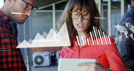 Reviewing woman wearing red button-down shirt holding tablet in office, with financial graphs....