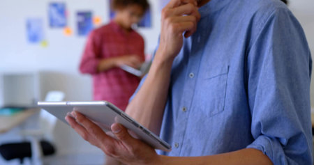 Asian male wearing blue shirt holding tablet resting chin in office, with sticky notes, copy space. Collaboration, brainstorming, productivity, modern, casual, workspace, communicationの写真素材