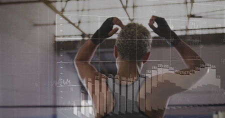 Raising arms female athlete standing in warehouse gym, with digital charts and fitness gloves. Sport, fitness, strength, wellbeing, performance, industrial, modernの写真素材