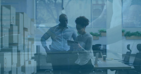 Examining tablet two colleagues standing by desk in open-plan office, with storage cabinets. Collaboration, teamwork, professionalism, modern, workspace, productivity, business casualの写真素材