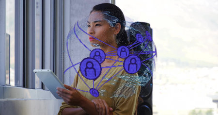 Woman in mustard blouse holding tablet at windows in office, with digital globe overlay and speaker. Technology, connectivity, collaboration, innovation, urban, professional, digitalの写真素材