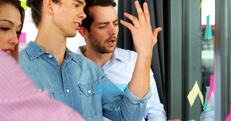 Gesturing man wearing denim shirt leading discussion in office, with glass sticky note partition. Collaboration, teamwork, innovation, brainstorming, creative, modern, professionalの写真素材