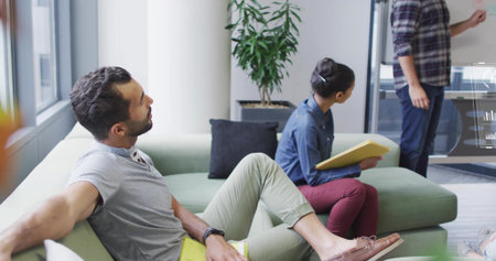 Collaborating four office colleagues sitting on green sofa in meeting area, using yellow folder....
