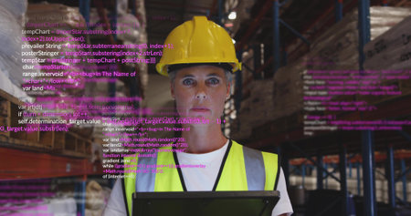 Warehouse manager wearing yellow hard hat, vest scanning tablet in warehouse, with code overlay. Industrial, logistics, organization, digital, efficiency, safety, technologyの写真素材