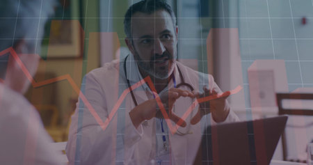 Explaining male doctor holding red pill organizer and gesturing in clinic, laptop data overlay. Healthcare, professionalism, analytics, wellness, consultation, medical, officeの写真素材