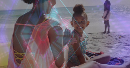 Mother and daughter playing on beach towels wearing swimsuits on shore, as father watching waves. Family, leisure, summer, happiness, seaside, relaxation, outdoorの写真素材