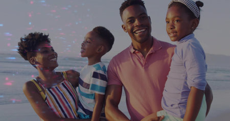 Smiling family holding children at sandy shoreline, with colorful outfits and calm ocean. Joy, togetherness, leisure, coastal, outdoor, happiness, bondingの写真素材