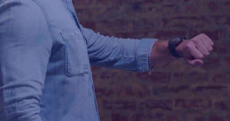 Checking man in denim shirt glancing at black smartwatch on exposed brick wall, showing textures. Urban, casual, textured, modern, lifestyle, minimalistic, deviceの写真素材