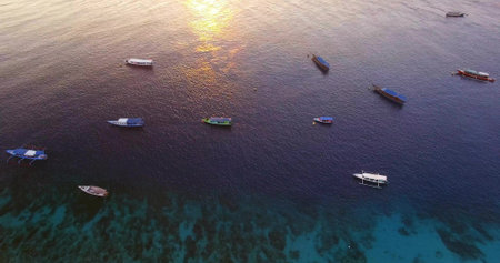 Floating white motorboat drifting over turquoise reef at sunrise, with colorful boats, copy space. Seascape, boating, tranquility, nautical, nature, adventure, scenicの写真素材