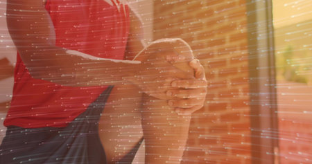 Massaging man wearing red sports shirt and black shorts in home gym, with sunlit brick wall. Recovery, wellness, fitness, exercise, relaxation, natural light, healthの写真素材