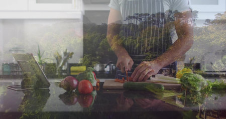 Chopping cook in apron arranging sliced vegetables on board in kitchen, with tablet showing forest. Vegetables, culinary, modern, lifestyle, minimalist, wellness, nourishmentの写真素材