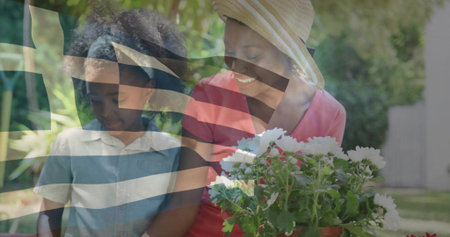 Holding terracotta pot of white daisies, woman wearing straw hat gardening with girl in backyard. Floristry, family, nurturing, outdoor, lush, vibrant, cheerfulの写真素材