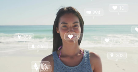 Standing woman wearing blue crochet top over pink bikini on beach, with floating social media icons. Beach, fashion, summer, lifestyle, vibrant, relaxation, outdoorの写真素材