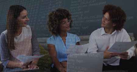 Three coworkers discussing network configuration overlay in office, with laptops and documents....