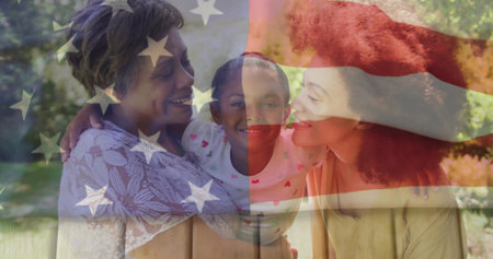 Embracing three-generation family smiling at each other in sunny park, with American flag overlay. Families, unity, patriotism, outdoor, wellness, connection, tranquilityの写真素材