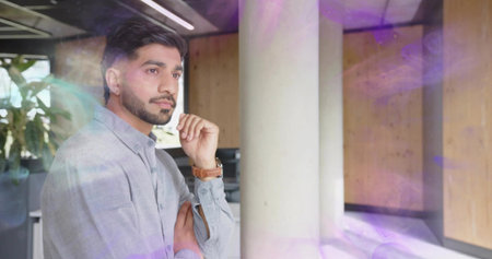 Leaning bearded man wearing grey shirt in office with white column and overhead lights, copy space. Professional, workspace, modern, interior, contemplative, corporate, minimalistの写真素材