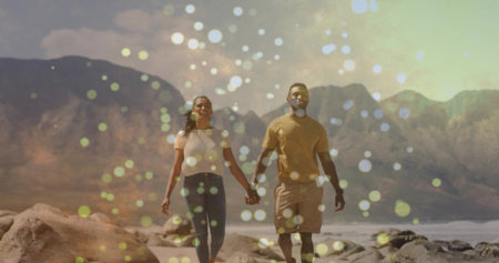 Walking couple wearing casual clothes across rocky shoreline, with mountain peaks and bokeh orbs. Adventure, romance, outdoor, scenic, leisure, nature, travelの写真素材