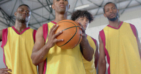 Holding basketball, four players wearing matching yellow-red jerseys on court under truss ceiling....