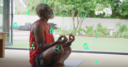 Meditating Senior man wearing orange top and smartwatch on yoga mat near glass door, floating icons. Meditation, mindfulness, wellness, nature, eco, serenity, lifestyleの写真素材