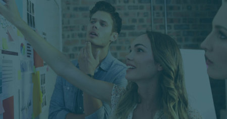 Pointing designer leading discussion on pinboard charts in modern studio, with focused teamwork. Collaboration, brainstorming, creativity, innovation, workspace, visualcommunication, teamworkの写真素材