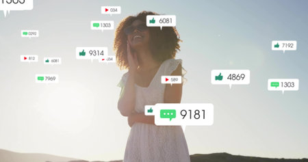 Holding smartphone near face, woman in lace dress standing on hillside at sunset, with social icons....