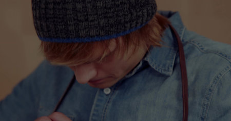 Adjusting male wearing blue beanie and denim shirt fastening leather suspenders against beige wall. Casual fashion, menswear, minimalism, wardrobe, street style, everydaywear, modernの写真素材