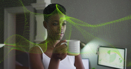 Holding ceramic mug woman wearing tank top in home office, with green swirl data on monitors....