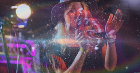 Shaking blonde musician wearing wide-brimmed hat performing on stage platform, with red tambourine. Live entertainment, stage performance, concert lighting, musical act, vibrant atmosphereの写真素材