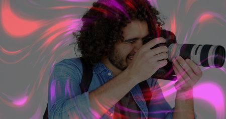 Aiming telephoto DSLR, photographer in denim shirt with backpack in studio, with pink-purple trails....