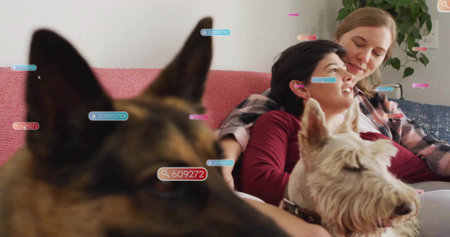 Sitting two mid adult women leaning on red sofa in living room, tracking labels and dogs. Affection,...
