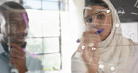 Collaborating man in shirt and woman in hijab planning on glass board at office, digital icons. Innovation, brainstorming, teamwork, modernity, productivity, technology, corporateの写真素材