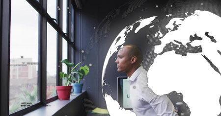 Leaning Asian man wearing white shirt gazing through office window with monitor, plant, copy space....