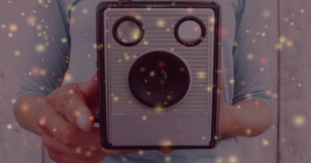 Holding adult woman positioning twin-lens camera against wooden wall, with floating ember specks....
