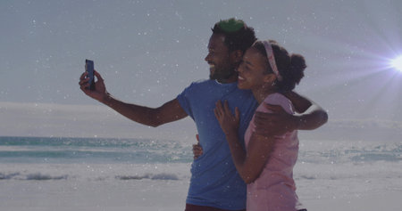 Taking selfie couple leaning into each other on sandy beach at sunset, with smartphone. Romantic, outdoor, leisure, serenity, sunshine, coastal, connectionの写真素材