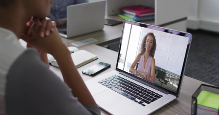 Displaying silver laptop showing woman speaking in virtual call at office, with wire mesh organizer. Collaboration, remote, communication, modern, professional, technology, workspaceの写真素材