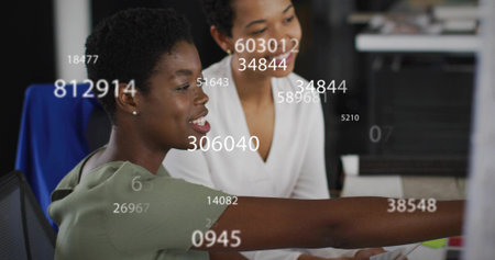 Pointing woman in green blouse analyzing monitor data at office desk with white blouse colleague. Business, teamwork, digital, collaboration, analytics, innovation, modernの写真素材