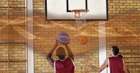 Holding basketball overhead, uniformed player preparing shot on gym court, with hoop, climbing bars. Athletes, teamwork, sport, training, fitness, competitive, youthの写真素材