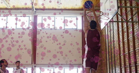 Dunking maroon jersey athlete sending basketball through rim on school gym court, copy space....