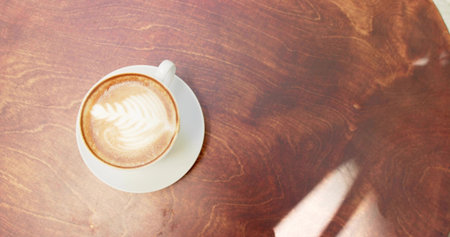 Showcasing white ceramic coffee cup sitting on polished wooden cafe table, with latte foam art. Minimalist, rustic, cozy, gourmet, beverage, hospitality, craftの写真素材