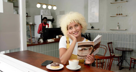 Reading woman wearing yellow dress leaning head on hand at cafe counter, with book and cappuccino....
