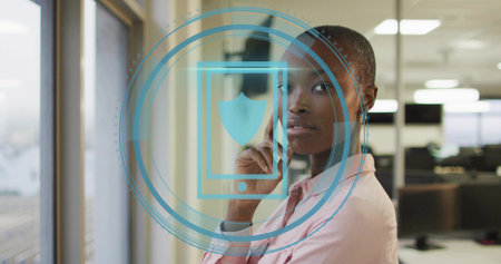 Standing woman in pink shirt gazing beside large window at open-plan office, with digital overlay....