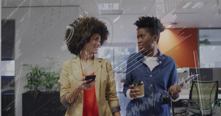 Walking two professional women discussing report in office corridor, with phone, tablet and coffee. Collaboration, teamwork, innovation, communication, modern, professional, technologyの写真素材