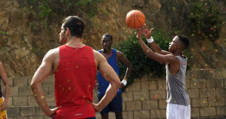 Man in gray sleeveless top with white shorts shooting basketball on outdoor court, copy space....