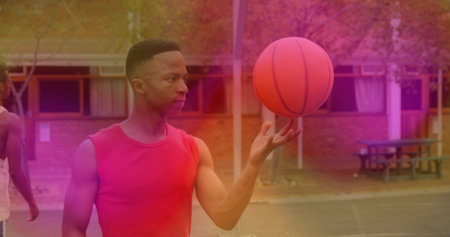 Man in red tank top spinning orange basketball on finger on asphalt court, copy space. Athletic, teamwork, outdoor, vibrant, leisure, fitness, communityの写真素材