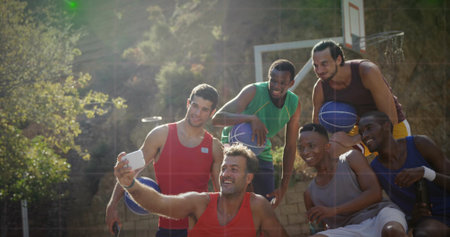 Six basketball teammates leaning around player holding smartphone in hardcourt, with balls and hoop. Athletics, camaraderie, outdoor, vibrant, activity, leisure, teamworkの写真素材