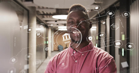 Smiling man wearing red shirt and dark pants in office corridor, showing holographic banking icons. Modern, professional, futuristic, finance, digital, corporate, innovationの写真素材