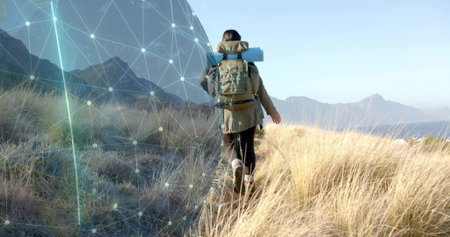 Hiking hiker carrying backpack with rolled mat through coastal grasses, with digital overlay....